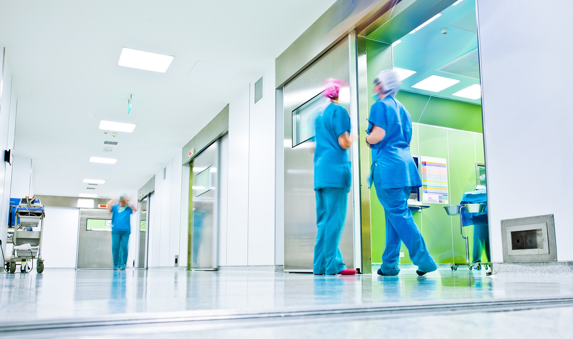 A busy hospital corridor with healthcare workers in scrubs. Two Locum Tenens CRNA interact by elevators, emphasizing a dynamic medical environment.