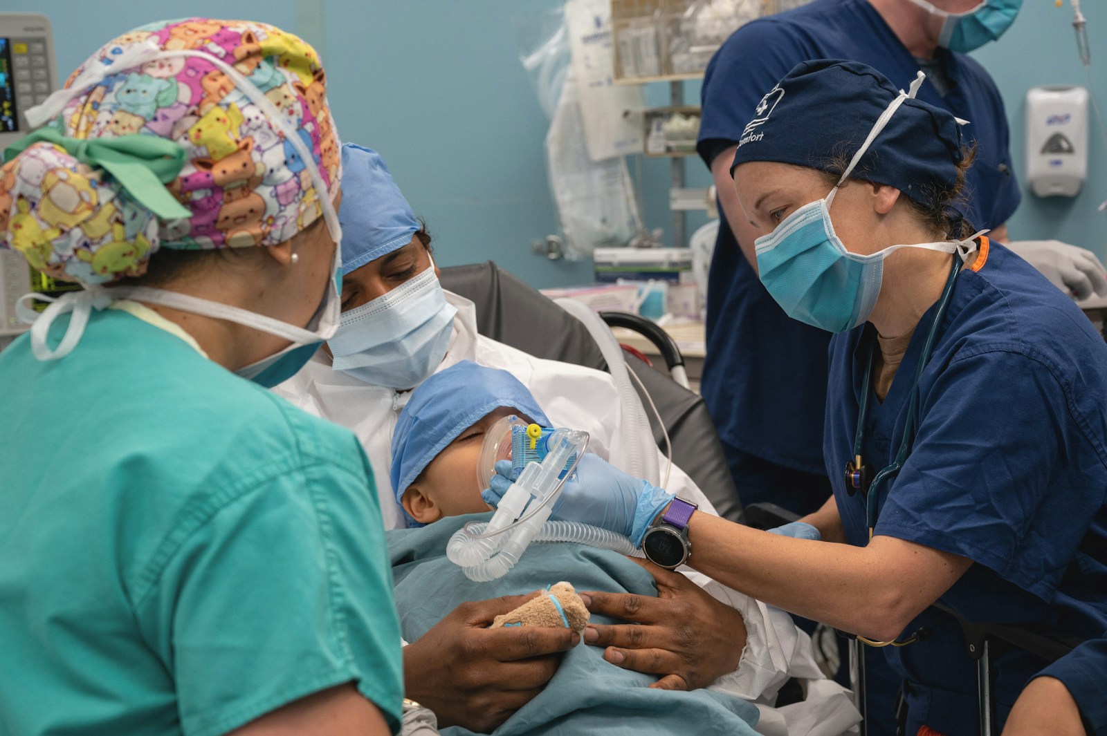 Healthcare professionals provide care to a young child in a medical setting using anesthesia equipment, assisted by a locum tenens CRNA while a parent offers comfort.